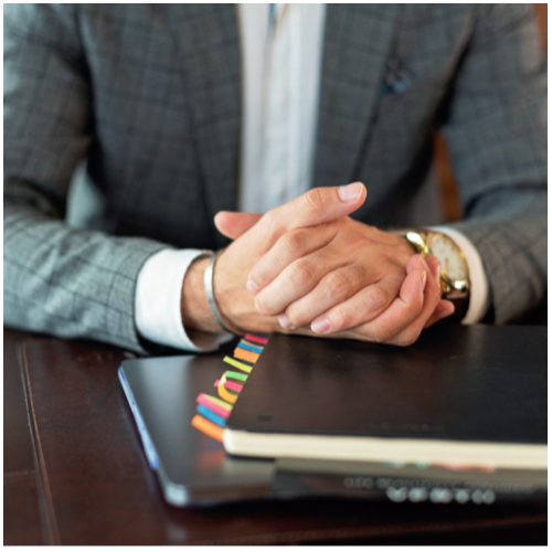 Professional in a suit waiting for an interview or meeting, hands resting on a notebook